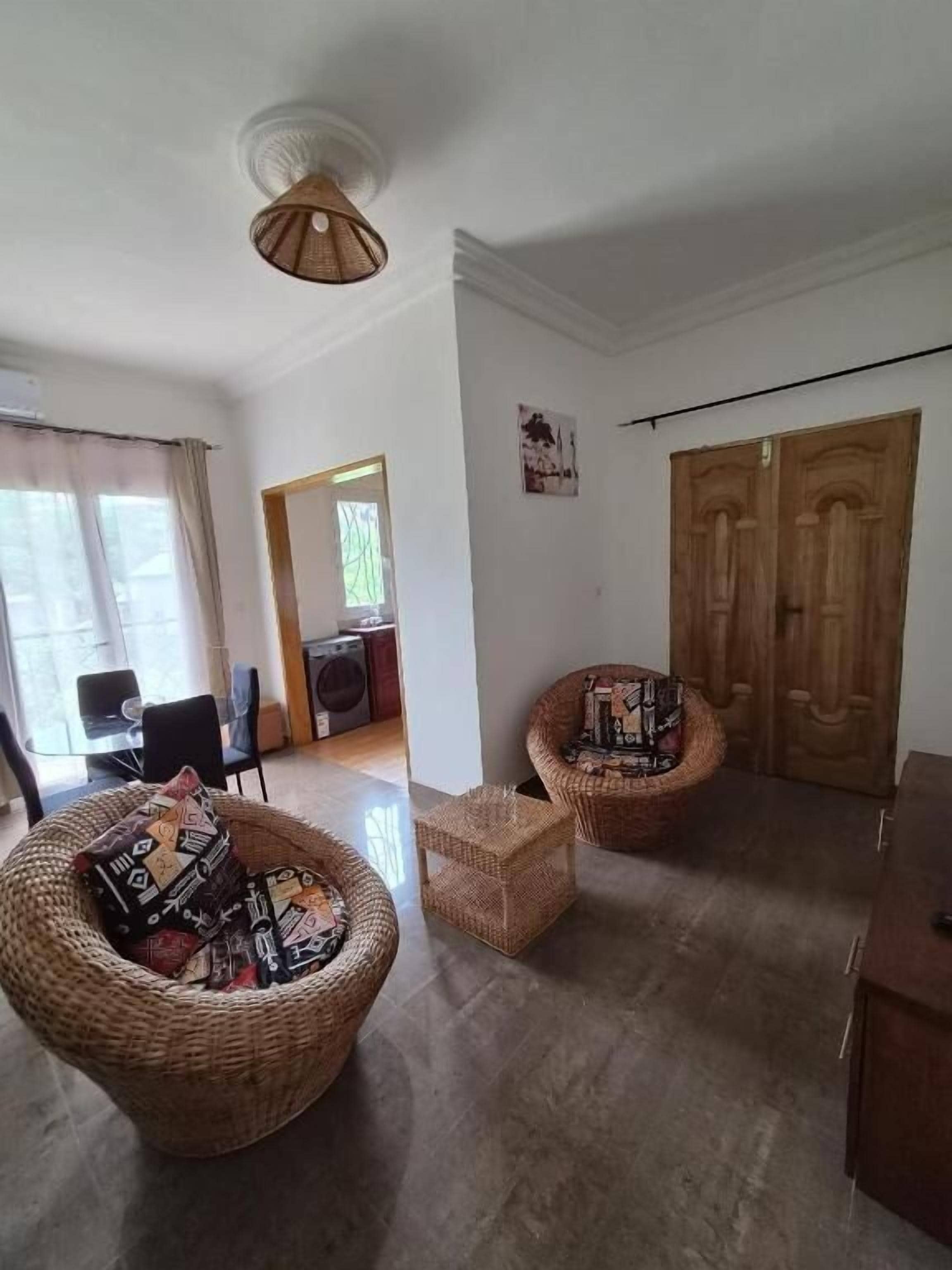 A room with two wicker chairs, a small table, a wooden cabinet, and a ceiling fan.