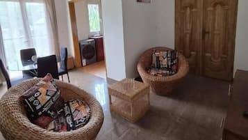 Una habitación con dos sillones de mimbre, una mesita, un armario de madera y un ventilador de techo.