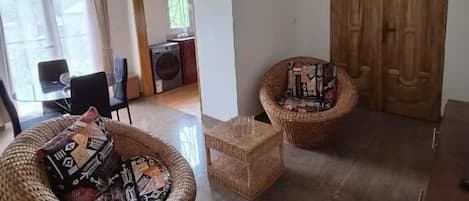 Una habitación con dos sillones de mimbre, una mesita, un armario de madera y un ventilador de techo.