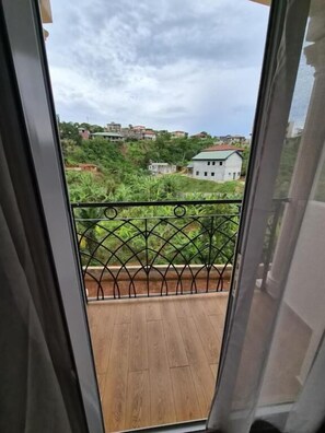 A balcony with a wooden floor and a metal railing, overlooking a residential area with houses and greenery.