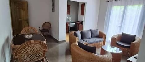 A spacious living area with wicker furniture, a wooden ceiling, and a view of the kitchen.