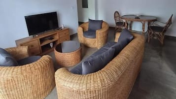 A living room with wicker furniture, a flat-screen TV, and a dining area with a round table and chairs.