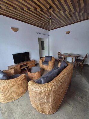 Una sala de estar con muebles de mimbre, un televisor de pantalla plana y un comedor con una mesa redonda y sillas.