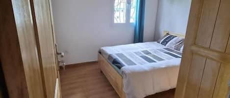 Un dormitorio con techo de madera, una cama con cubrecama blanco, una ventana con cortinas azules y un armario de madera.
