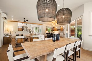 Un'ampia zona giorno con un grande tavolo da pranzo in legno, lampade a sospensione moderne e vista sulla cucina e sullo spazio esterno.