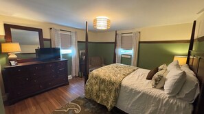 Une chambre à coucher avec un lit, une commode, un téléviseur et une fenêtre avec des rideaux.