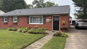 Une maison à deux étages, construite en briques, avec une porte d’entrée noire, le numéro 722, et un petit jardin devant la maison où poussent différentes plantes.