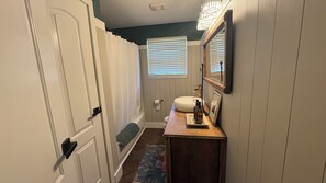 Un couloir étroit avec une porte, une fenêtre avec des stores, un lavabo avec un miroir et un banc en bois.
