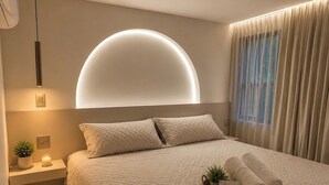 Quarto moderno com uma cama grande, mesa de cabeceira com planta e luminária fixada na parede.