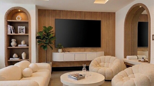 Uma sala de estar moderna com uma grande televisão de tela plana, duas mesas de centro redondas e duas poltronas confortáveis.