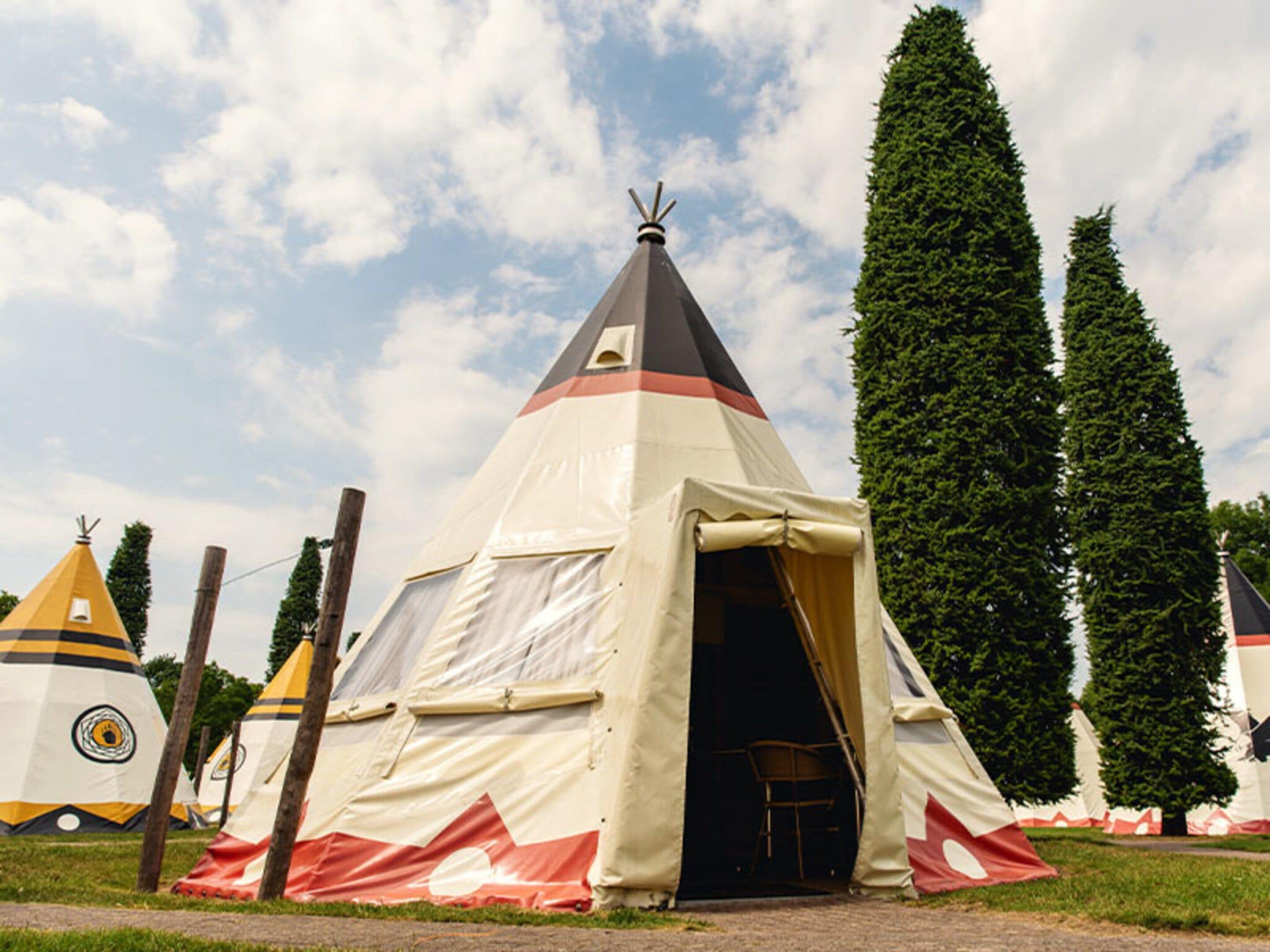 A conical tent with a door open, surrounded by trees and other tents.