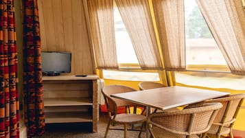 A room with a television on a shelf, wicker chairs, a table, and a window with curtains.