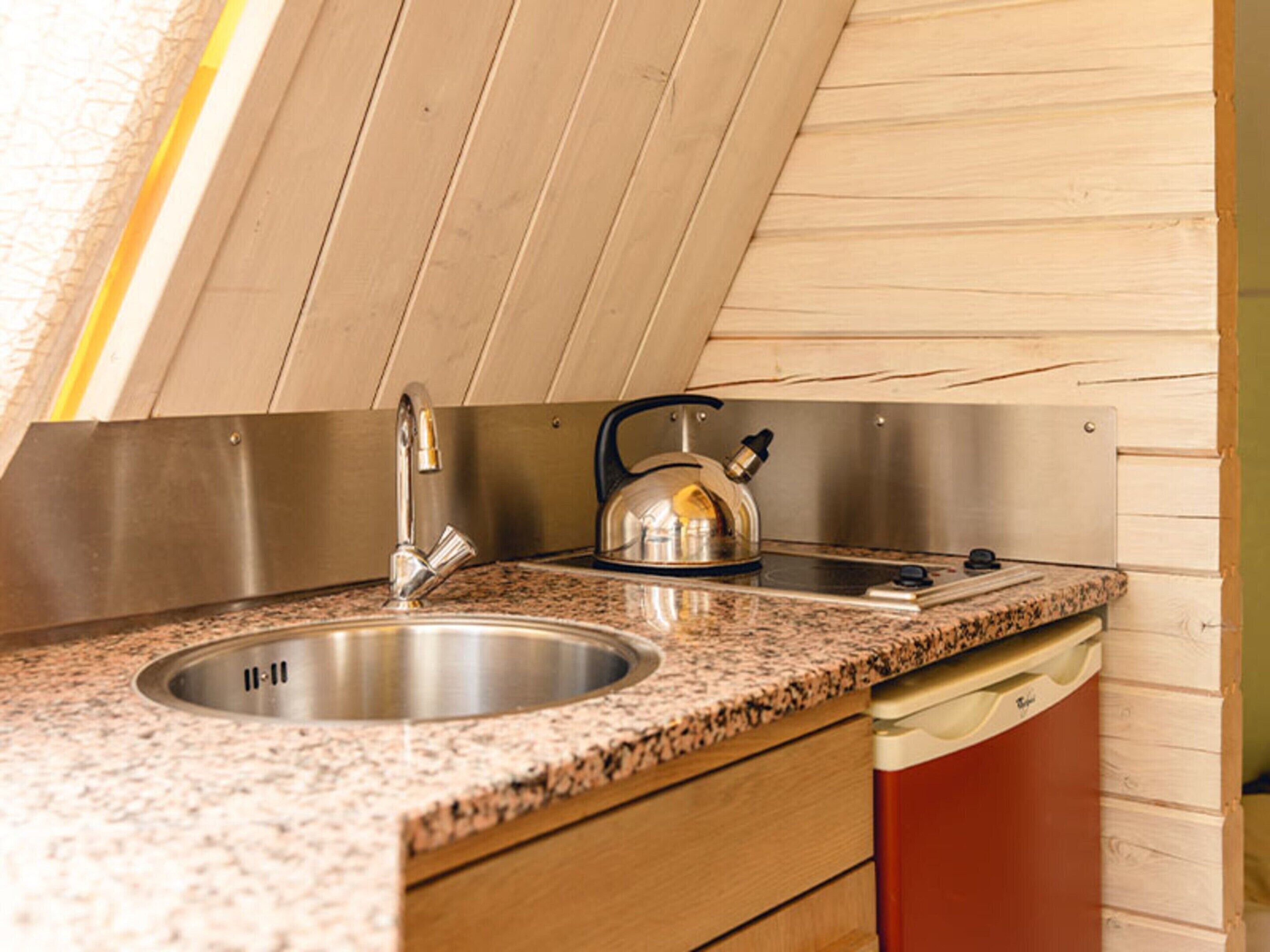 A kitchen with a stainless steel sink, a kettle, and a dishwasher.