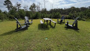 Ein Außenbereich mit Adirondack-Stühlen und einem Picknicktisch, umgeben von Gras und Bäumen.