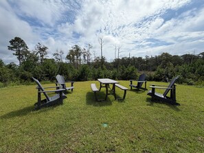 Un espacio exterior con sillas Adirondack y una mesa de picnic, rodeado de césped y árboles.