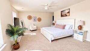 Ein Schlafzimmer mit einem Bett, einem Sessel, einem Schreibtisch, einem Deckenventilator und einem an der Wand montierten Fernseher.
