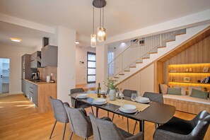 Een moderne keuken met een inbouwoven, een eethoek met een lange tafel en stoelen, en een trap naar een vide.
