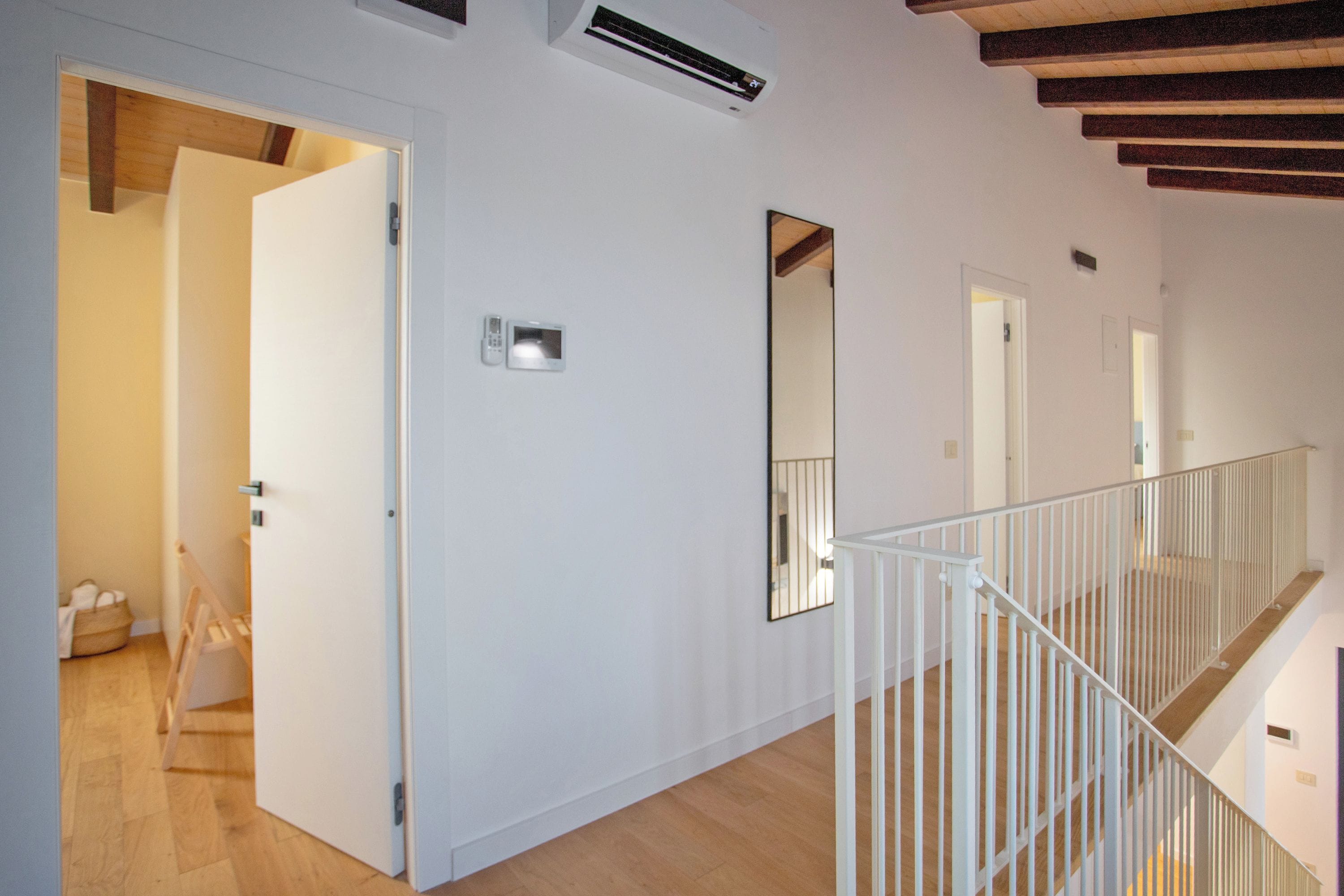 Un interior moderno con piso de madera, paredes blancas, una escalera con barandilla blanca y un equipo de aire acondicionado instalado en la pared.