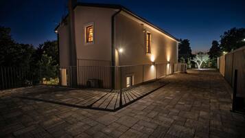 Un edificio de dos pisos con un patio empedrado, una entrada con portón y un ventanal en el nivel superior.