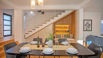 Un comedor con una mesa dispuesta para cuatro, una escalera y una sala de estar con sofá y estanterías.