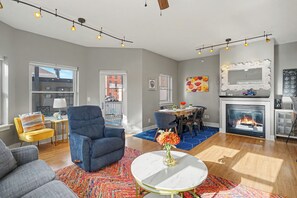 Ein modernes Wohnzimmer mit Kamin, Essbereich und durchgehender Tür sichtbarer Küche.