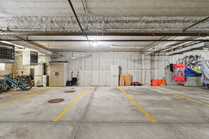 A parking garage with concrete floors, yellow parking lines, and various items like bicycles, a motorcycle, and storage boxes. - Downtown condo with pool and parking (South Haven)