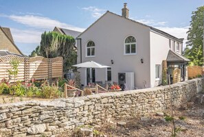 A two-story house with a stone wall in front, a patio with outdoor furniture, and a garden with various plants. - Old Chapel in the heart of South Cerney, charming house with a beautiful garden (South Cerney)