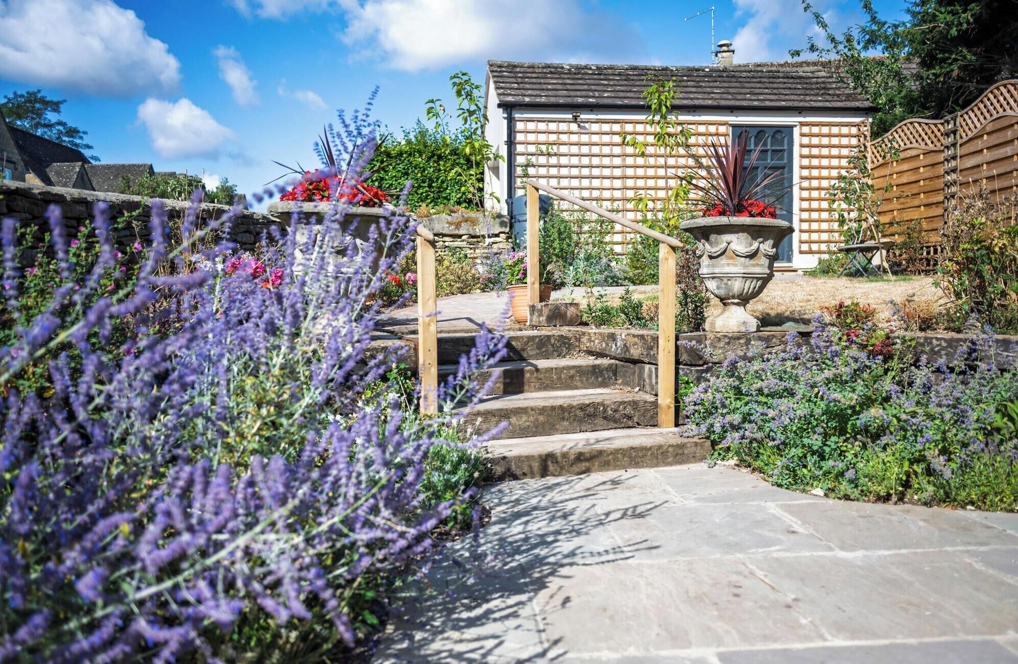 A stone staircase leading to a house with a wooden fence and a garden with lavender plants.
