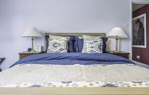 Una cama con colcha azul y dos almohadas estampadas, con mesitas de noche y lámparas a cada lado.