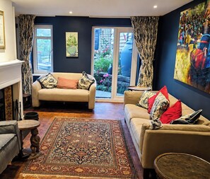 A living room with two sofas, a patterned rug, and a large painting on the wall. - Old Chapel in the heart of South Cerney, charming house with a beautiful garden (South Cerney)