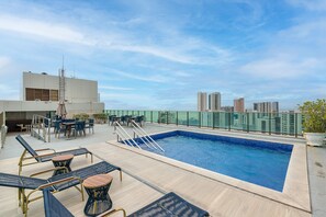 A rooftop pool area with lounge chairs, a table, and a view of the city skyline. - Aparament em Boa Viagem-Prox a Praia-167 (Recife)