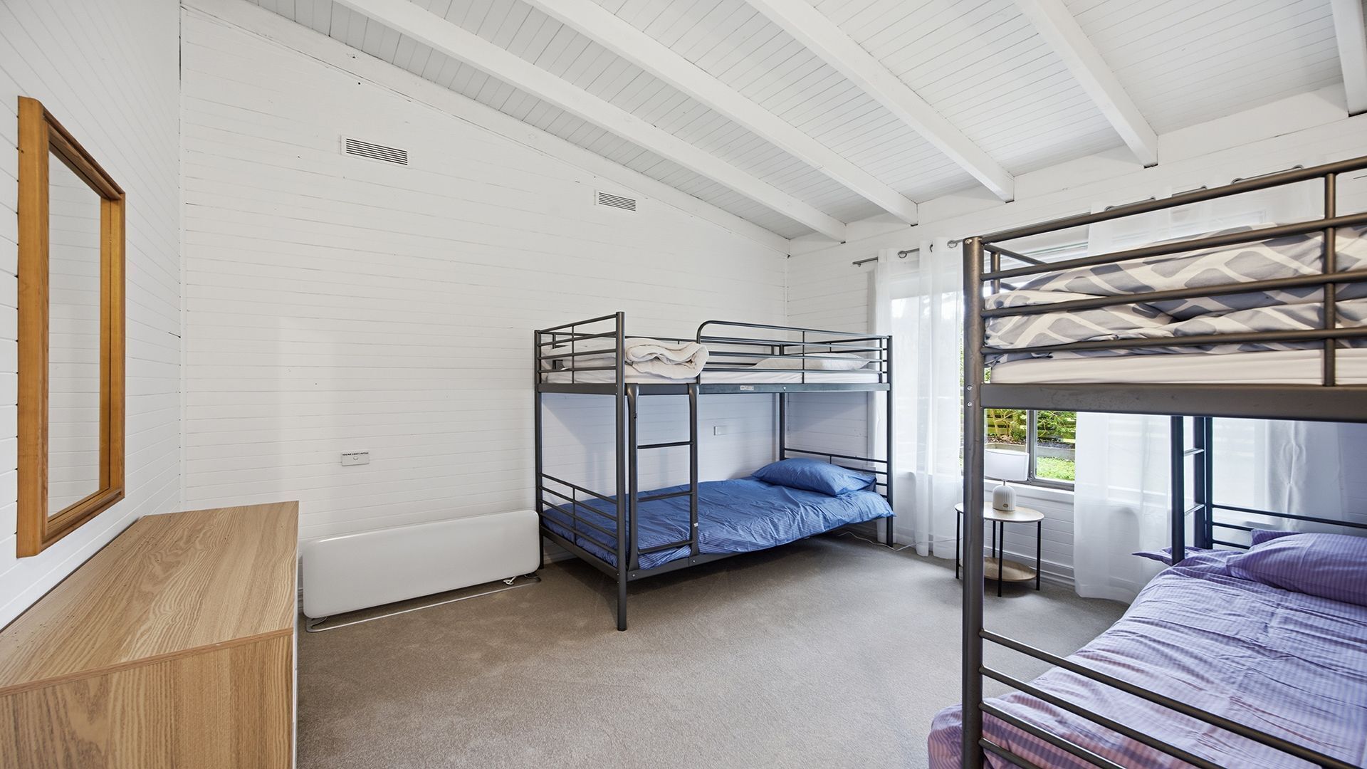 Dormitorio con literas, paredes blancas, suelo de madera y una ventana con cortinas.