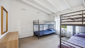 Dormitorio con literas, paredes blancas, suelo de madera y una ventana con cortinas.