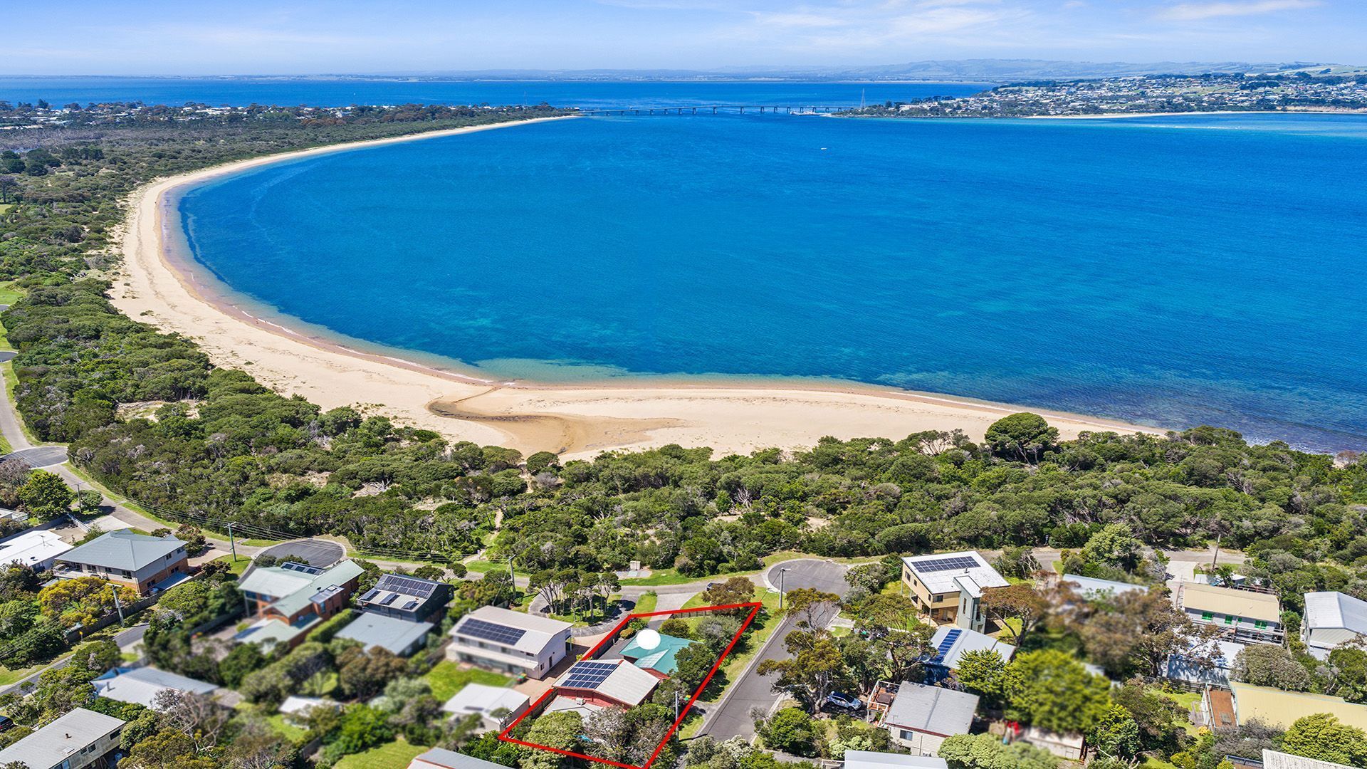 Vista aérea de una propiedad costera con acceso directo a la playa, abundante vegetación y edificios residenciales.