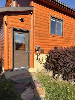 Una cabaña de troncos con puerta principal, ventana y un pequeño porche.