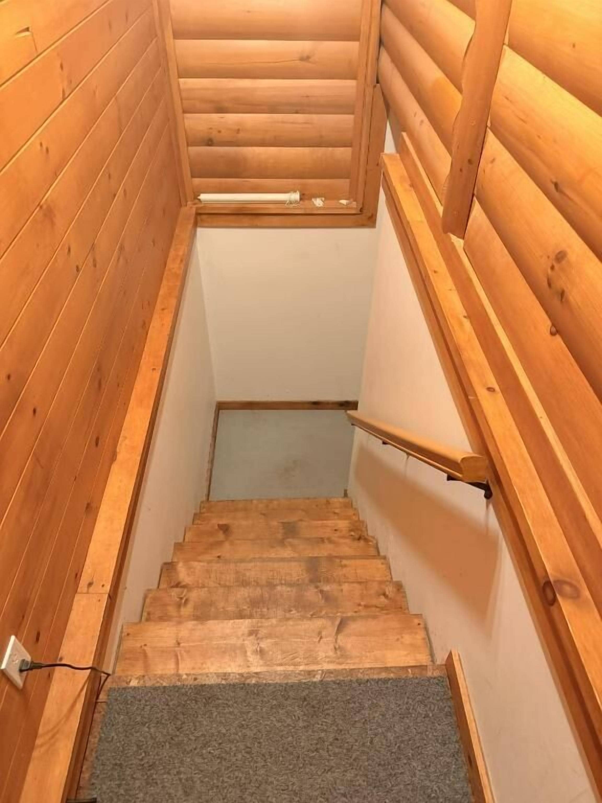 Un escalier en bois avec une rampe, des marches recouvertes de moquette et une fenêtre en haut.