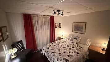 Ein Hotelzimmer mit Bett, Nachttischlampen, einem Tisch mit Lampe, einem Sessel und einem Fenster mit Vorhängen.
