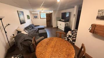 A living room with a round wooden table, a sofa, a television, and a cross on the wall.