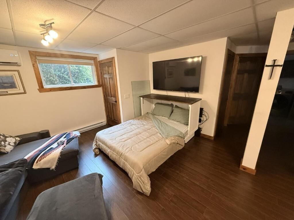 Un dormitorio con cama, televisor montado encima, ventana y puerta.