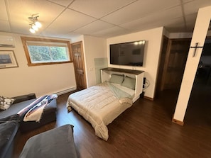 Un dormitorio con cama, televisor montado encima, ventana y puerta.