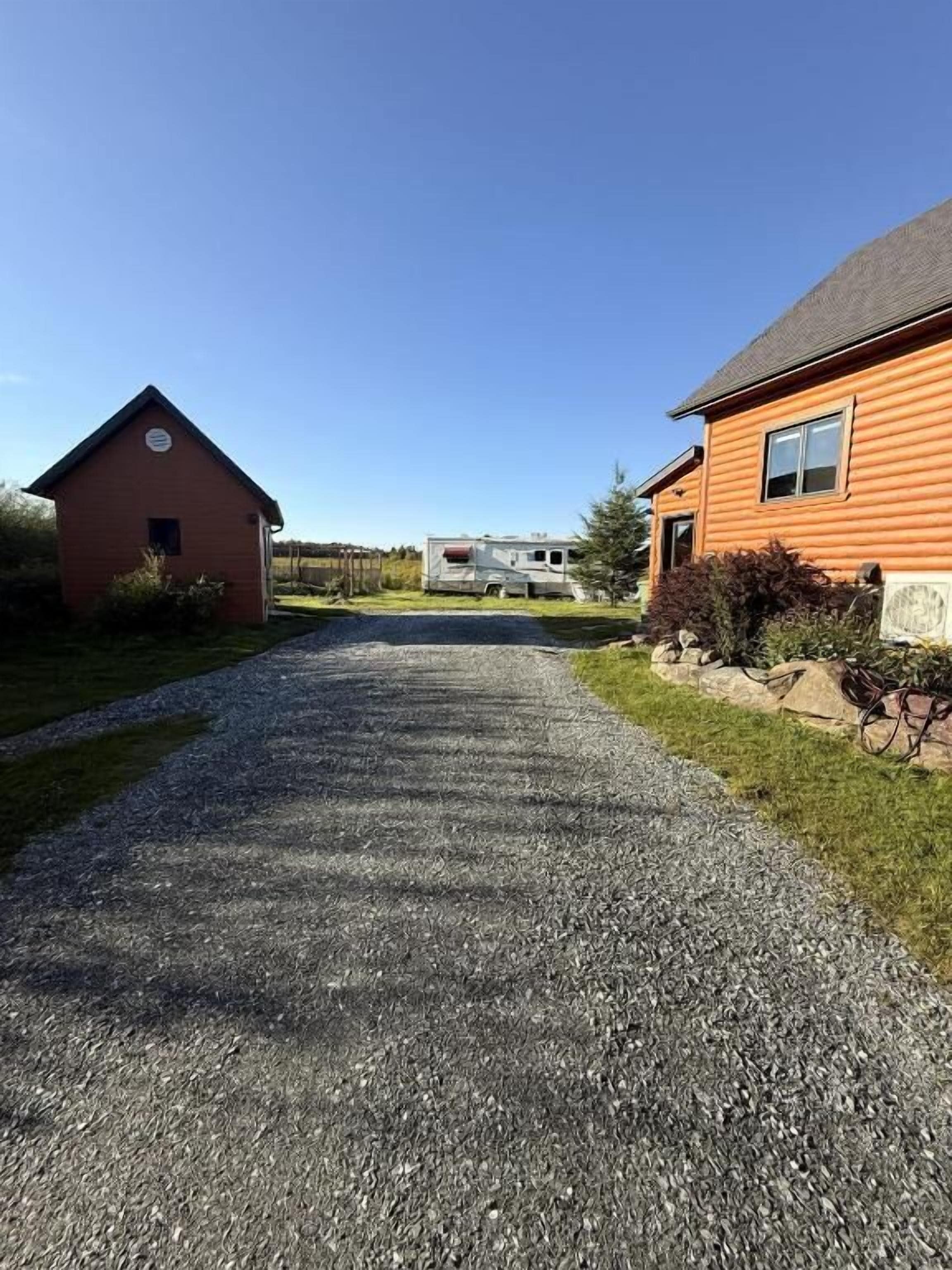 Un chemin de gravier mène à une grange rouge et à une grande maison orange, avec un ciel bleu dégagé au-dessus.