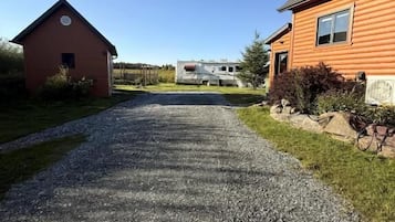 Un chemin de gravier mène à une grange rouge et à une grande maison orange, avec un ciel bleu dégagé au-dessus.