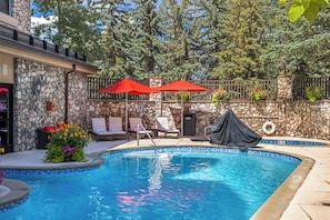 A swimming pool with lounge chairs and umbrellas, surrounded by stone walls and trees. - 411 Beaver Creek Lodge at the Covered Bridge, Pool, Hot Tub, Gym, Steam Room (Beaver Creek)