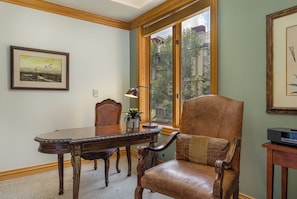 A room with a wooden dining table, a leather chair, a framed picture on the wall, and a window with a view of buildings. - 411 Beaver Creek Lodge at the Covered Bridge, Pool, Hot Tub, Gym, Steam Room (Beaver Creek)