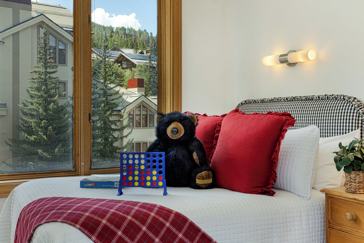 Un dormitorio con un ventanal grande, un osito de peluche, un rompecabezas y un cabecero a cuadros.