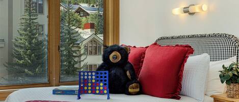 Un dormitorio con un ventanal grande, un osito de peluche, un rompecabezas y un cabecero a cuadros.