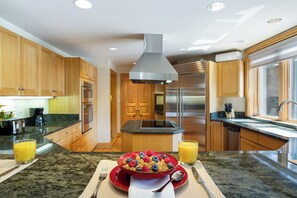 A modern kitchen with wooden cabinets, stainless steel appliances, granite countertops, and a breakfast setup with cereal and fruit. - 411 Beaver Creek Lodge at the Covered Bridge, Pool, Hot Tub, Gym, Steam Room (Beaver Creek)