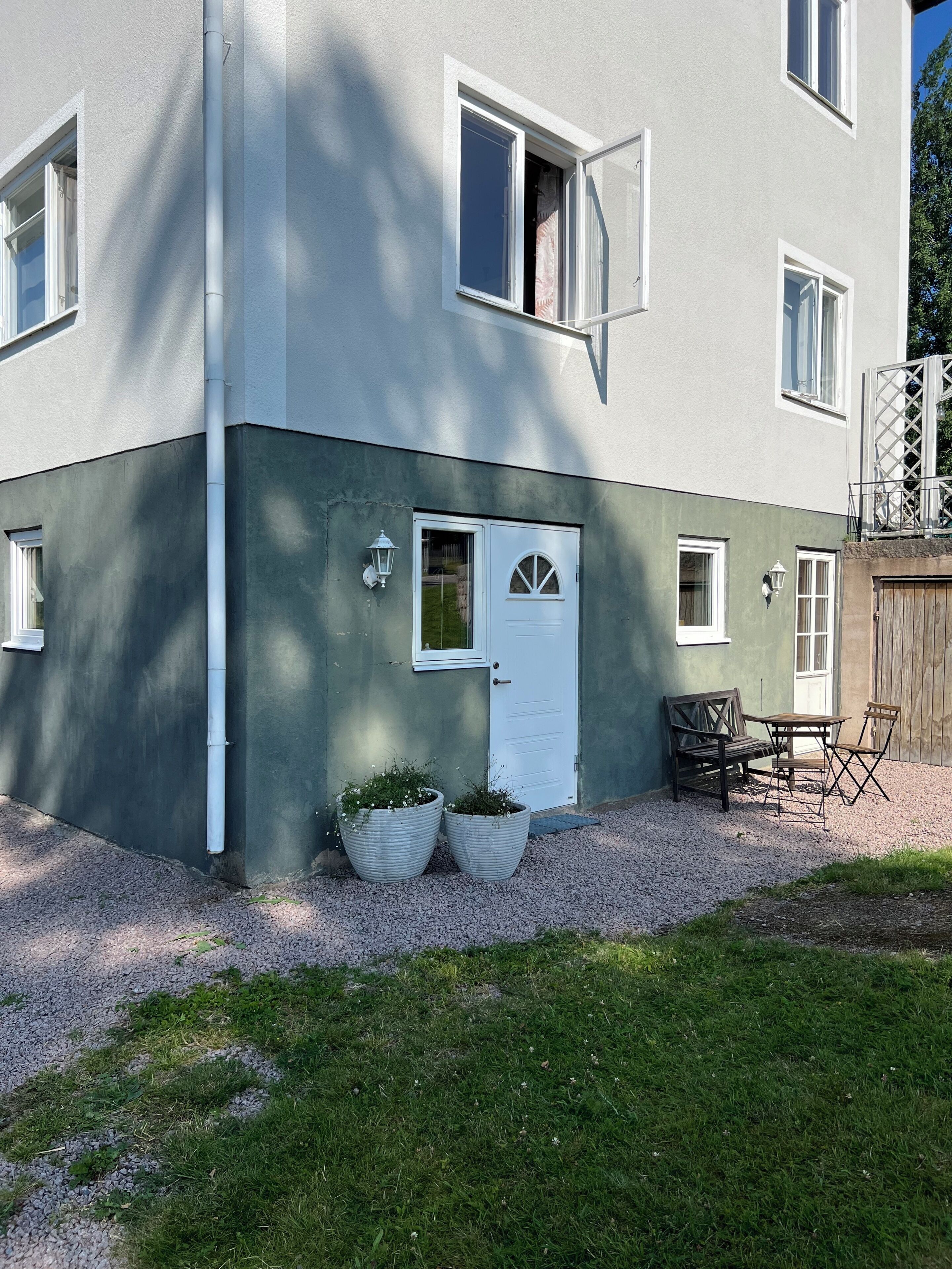En tvåvåningsbyggnad med en vit dörr, två fönster och en liten uteplats med ett bord och stolar.