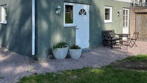 Un bâtiment à deux étages avec une porte blanche, deux fenêtres et un petit patio comprenant une table et des chaises.