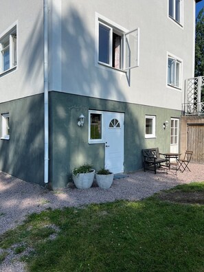 A two-story building with a white door, two windows, and a small patio with a table and chairs. - Sjöbacken – Lovely apartment in the heart of Braås (Braås)